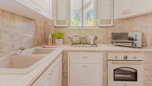 Une cuisine équipée d’un évier, d’une cuisinière, d’un four et d’une fenêtre située au-dessus du plan de travail.