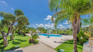 Un espace piscine avec un ciel dégagé, entouré d’arbres et doté d’un coin salon abrité.