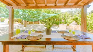 Une table en bois, dressée pour quatre personnes, avec un pot d’aloe vera placé au centre, entouré de sets de table en fibres tressées et de verres transparents remplis d’une boisson jaune.