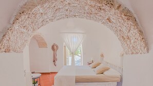Une chambre à coucher avec un lit, une petite table sur laquelle est posée une plante, et une fenêtre avec des rideaux.