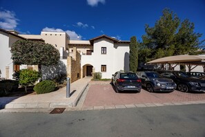 A two-story building with a white facade, a brown roof, and a driveway with parked cars. - Zc02 Adjacent to Aphrodite Hills- Communal Pool, Garden (Kouklia)
