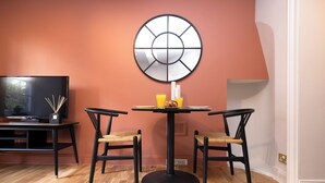 Un comedor con una mesa redonda, dos sillas, un televisor y un reloj en la pared.