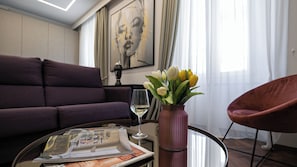 A living room with a purple sofa, a glass coffee table with a newspaper, a vase with yellow tulips, a wine glass, and a painting on the wall.