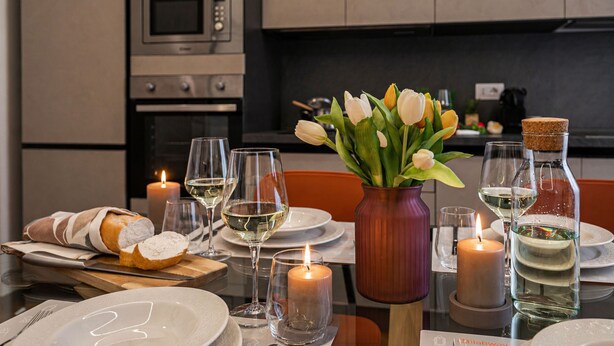 Een eettafel gedekt met borden, glazen, kaarsen, een vaas met bloemen en een brood.