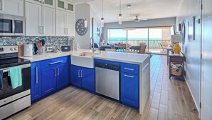 A modern kitchen with blue cabinets, a dishwasher, and a large window overlooking a balcony. - Prime Ocean Front at Sonoran Sun W602 (Puerto Peñasco)