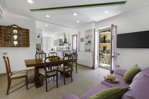 A modern living room with a dining area, a sofa, and a TV mounted on the wall. - ROSE SORRENTO HOUSE (Sorrento)