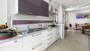 Uma cozinha moderna com armários brancos e roxos, um backsplash revestido de azulejos e um espaço de refeições com mesa e cadeiras.