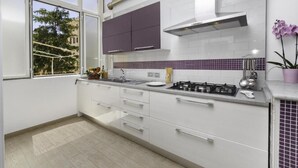 Cozinha moderna com armários brancos, fogão a gás e janela com vista para árvores.