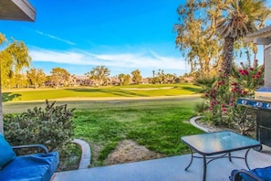 A patio with a view of a golf course, a grill, and a small table.