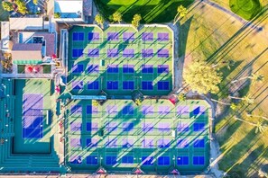 An aerial view of a sports complex with multiple tennis courts, a swimming pool, and surrounding greenery. - Fairway Retreat | 2BR Resorter (Palm Desert)