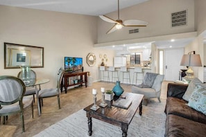 A spacious living room with a dining area, a kitchen in the background, and a ceiling fan.