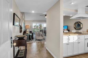 A modern kitchen with white cabinets, a large island, and a dining area with a chair and table.