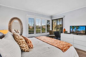A bedroom with a large bed, a mirror, a television, and a view of a golf course through the windows.