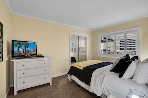 A bedroom with a bed, a dresser, a television, and a window with blinds.