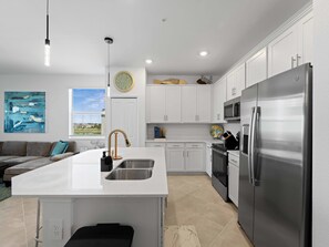 A modern kitchen with white cabinetry, a stainless steel refrigerator, a built-in oven, and a large island with a sink. - Wellen Park Golf Condo Balcony, Golf View - Pool - (Venice)