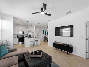 A modern kitchen with white cabinets, a central island, and a dining area with a TV mounted on the wall.