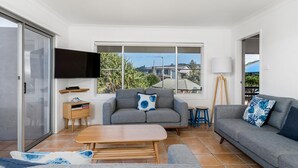 A modern living room with a grey sofa, a wooden coffee table, and a TV mounted on the wall. - Absolute Beachfront Apartment 4T (Lennox Head)