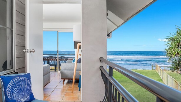 A balcony with a view of the ocean, a door leading to an interior space, and a chair with a blue cushion. - Absolute Beachfront Apartment 4T (Lennox Head)