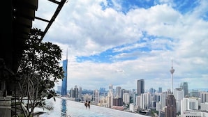 Une piscine à débordement située sur le toit, offrant une vue panoramique sur la ville, notamment sur une tour emblématique et le bâtiment Grand Millennium.