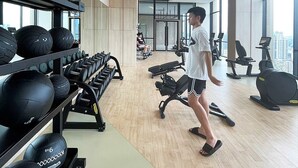 Une salle de sport moderne, dotée d’équipements d’exercice, de grandes fenêtres et offrant une vue sur la ville.