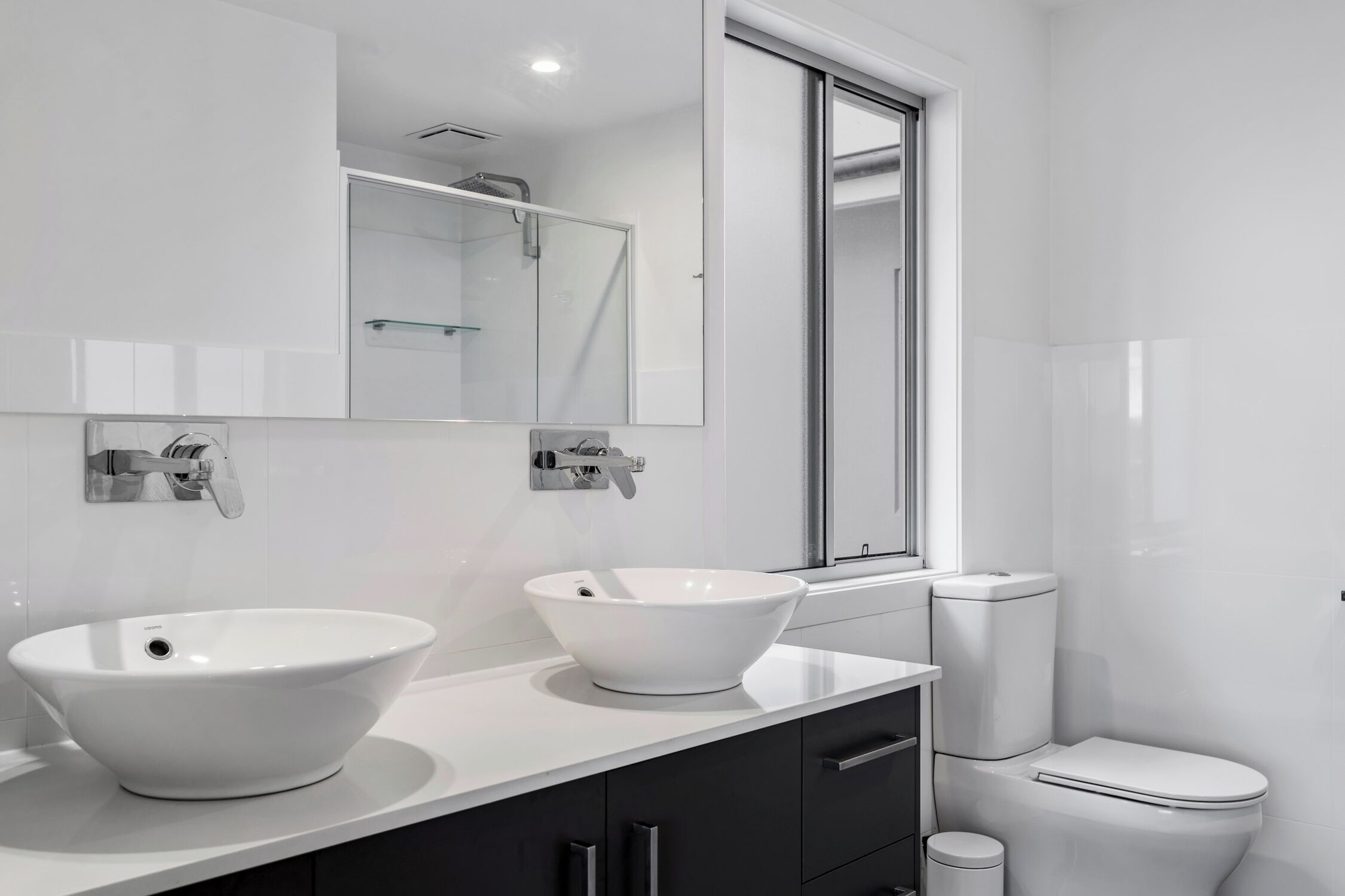Un baño moderno con un lavamanos grande blanco, un espejo y un inodoro.