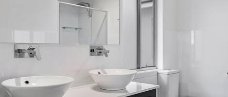 Un baño moderno con un lavamanos grande blanco, un espejo y un inodoro.