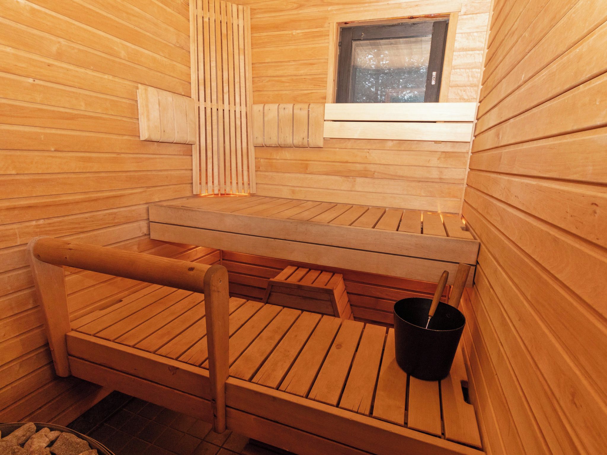 A sauna with wooden benches, a window, and a bucket.