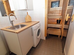 A compact kitchen with a washing machine, a sink, and wooden storage shelves. - Petsukka by Interhome (Kittilä)