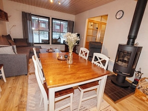 A cozy living room with a wooden dining table, white chairs, a vase of flowers, and a wood-burning stove.