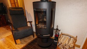 A modern room with a wood-burning stove, a comfortable chair, and a basket of firewood. - Petsukka by Interhome (Kittilä)