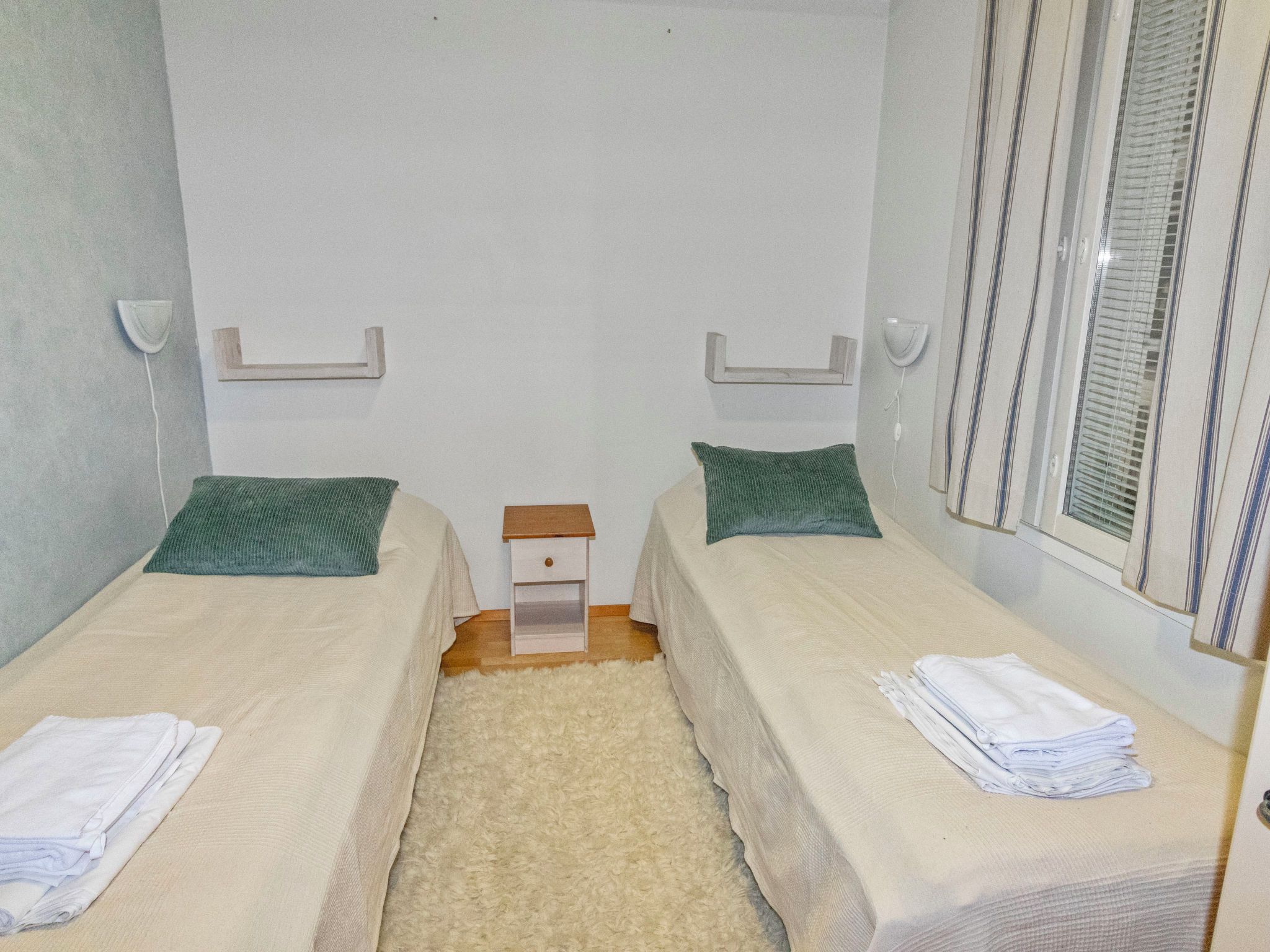 Habitación doble con dos camas, una mesita de noche pequeña y una ventana con persianas.