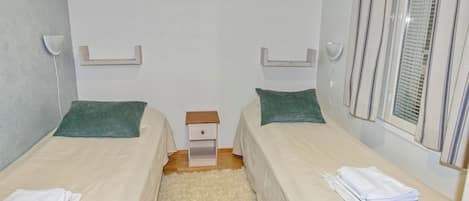 Habitación doble con dos camas, una mesita de noche pequeña y una ventana con persianas.