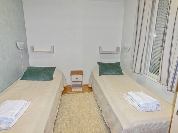 Habitación doble con dos camas, una mesita de noche pequeña y una ventana con persianas.