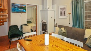 Una sala de estar acogedora con una mesa de comedor de madera, un sofá y un televisor montado en la pared.