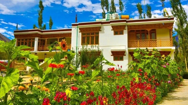 A two-story building with a balcony and a garden with colorful flowers. - Hotel Ldumra Oasis (Leh)
