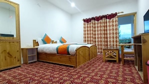A bedroom with a bed, a wooden desk, a television, and a window with curtains. - Hotel Ldumra Oasis (Leh)