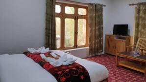 A hotel room with a bed, a television on a wooden cabinet, a desk with a chair, and a window with curtains. - Hotel Ldumra Oasis (Leh)