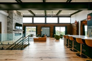 Un amplio salón con chimenea de piedra, una escalera de madera y una zona de bar con taburetes.
