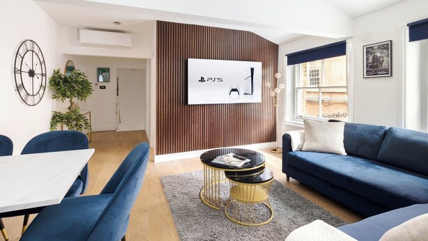 Ein modernes Wohnzimmer mit Flachbildfernseher, blauen Möbeln, einer Essecke und einer Wand mit Holzverkleidung.
