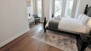 Ein Schlafzimmer mit einem großen Bett, einem Schreibtisch und zwei Fenstern mit Vorhängen.