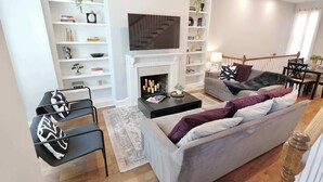 Ein Wohnzimmer mit Kamin, einer Couch, einem Couchtisch und einem Fernseher, der über dem Kamin angebracht ist.