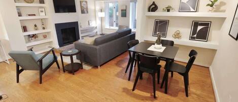 A modern living room with a fireplace, a sofa, a dining table with chairs, and a TV mounted on the wall.
