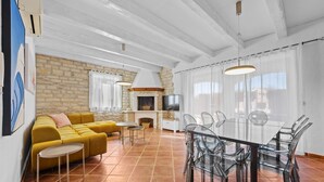 Una sala de estar moderna con pared de piedra, sofá amarillo, mesa de comedor de cristal y chimenea.