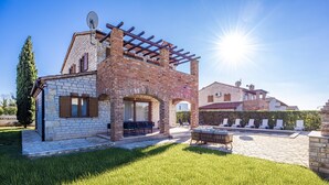 Una casa de dos pisos con fachada de piedra, una pérgola y un patio amueblado al aire libre.