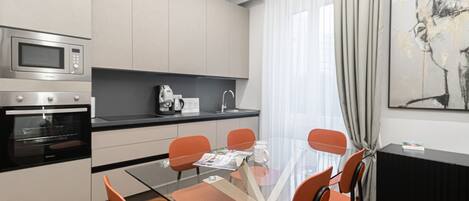 A modern kitchen with a microwave, oven, and coffee maker. There is a dining table with chairs and a glass top.