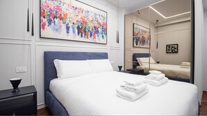 Habitación de hotel moderna con una cama grande, una mesita de noche, un espejo y un cuadro abstracto de colores en la pared.