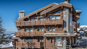 Ein mehrstöckiges Holzhaus mit Balkonen, Steinwänden und Blick auf schneebedeckte Berge.