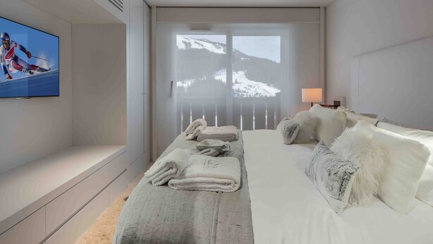 Ein Hotelzimmer mit Bett, Fernseher, einem Balkon mit Blick auf verschneite Berge und einem Fenster mit Bergblick.