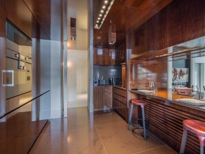 A modern kitchen with a wooden countertop, two stools, and a large mirror.