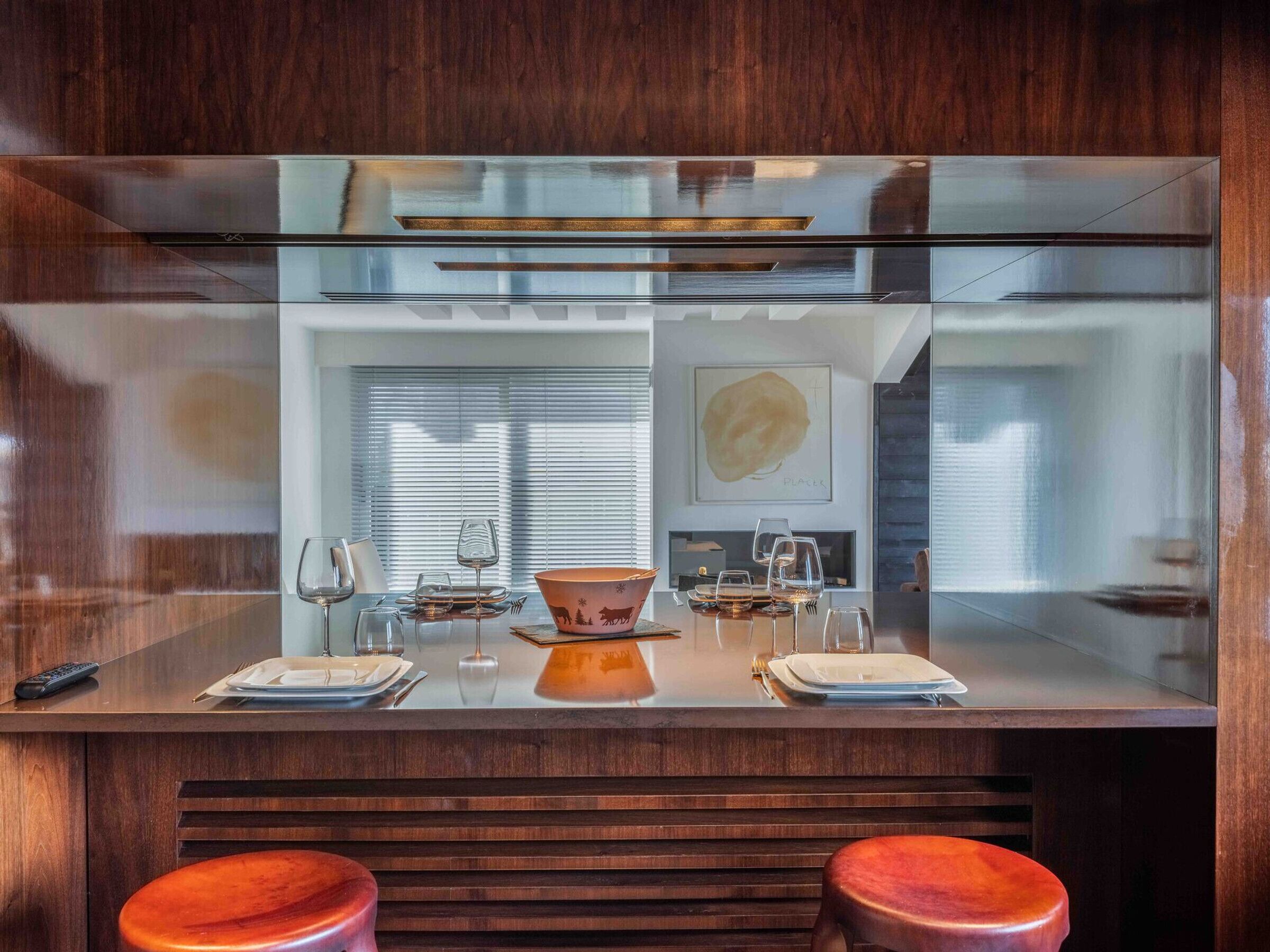 A modern kitchen with a central island, wooden bar stools, and a large window with blinds.